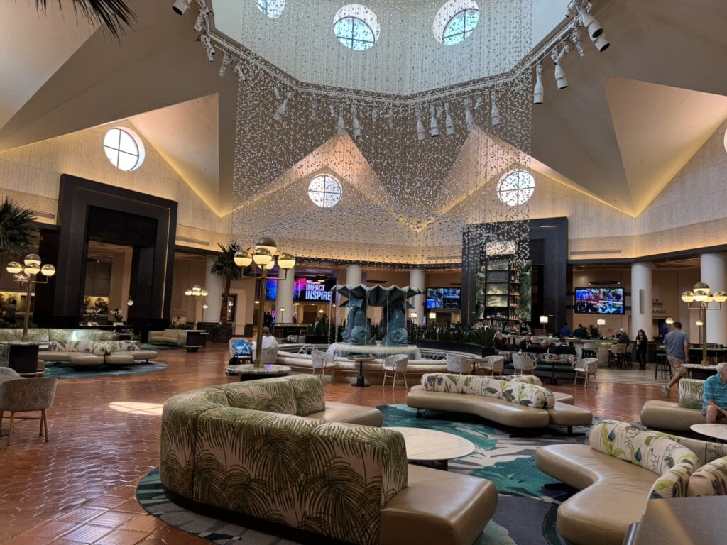 The spacious lobby of the Walt Disney World Dolphin Hotel features palm-patterned seating, elegant lighting, a grand chandelier, and multiple lounge areas.