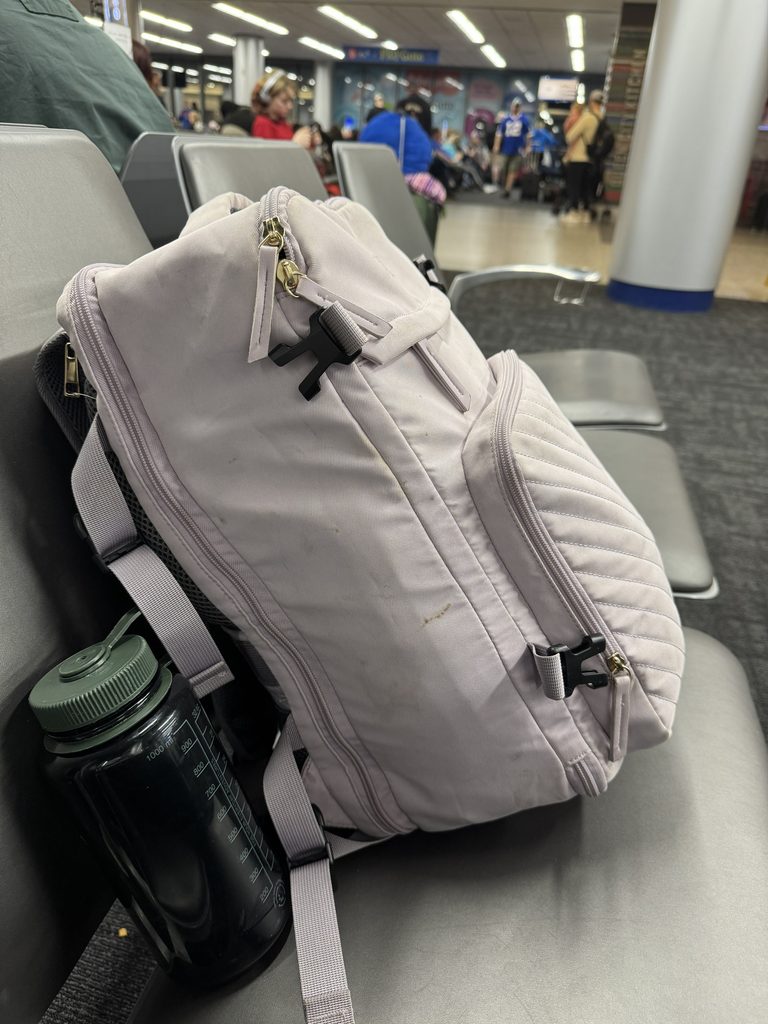 Personal-item backpack for flying with kids sitting at the airport, with a reusable water bottle beside it
