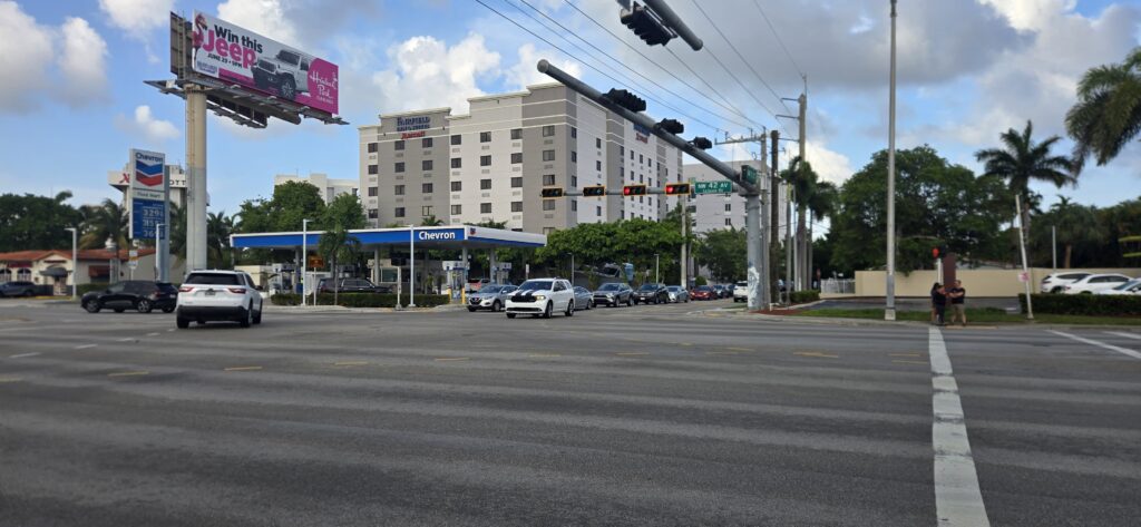 Street view of the Fairfield Inn & Suites Miami Airport South, a multi-story hotel situated behind a Chevron gas station at the busy intersection of NW 42nd Avenue and NW 11th Street in Miami, Florida.