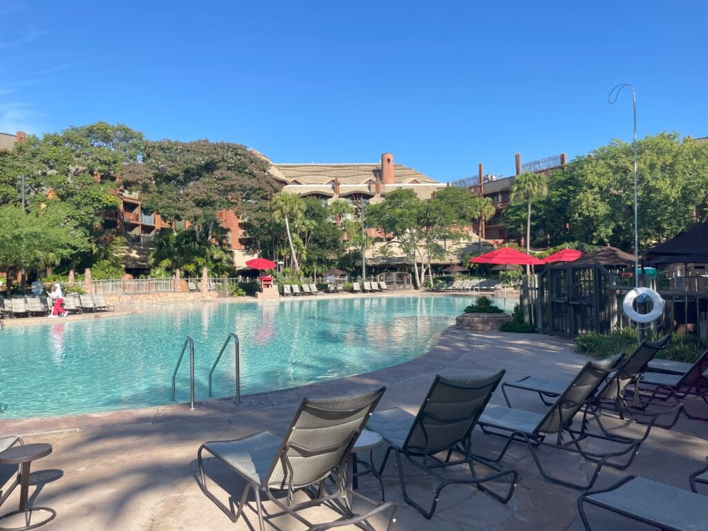 Wide view of the Uzima Springs Pool at Animal Kingdom Lodge, featuring a zero-entry area, lounge chairs, and red umbrellas.