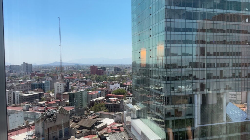 A panoramic view of Mexico City from a high-rise window at Le Méridien, with a sleek glass building reflecting the urban sprawl below.