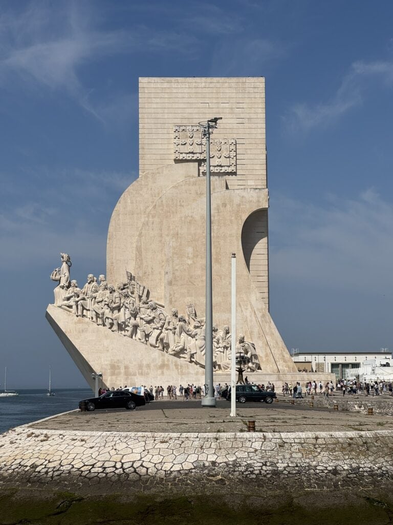 Wide shot of Padrão dos Descobrimentos rising over the waterfront on a bright sunny day, seen from across the marina during a family walk in Lisbon.