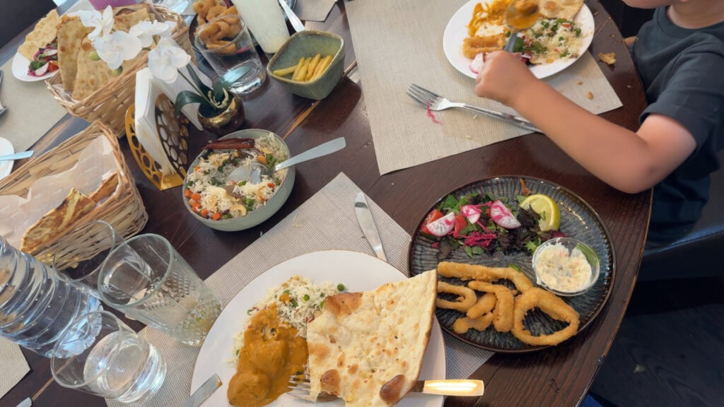 Table spread at Aroma da Índia in Lamego with naan, basmati rice, curry, fried calamari, and salad, with a child eating at the table.