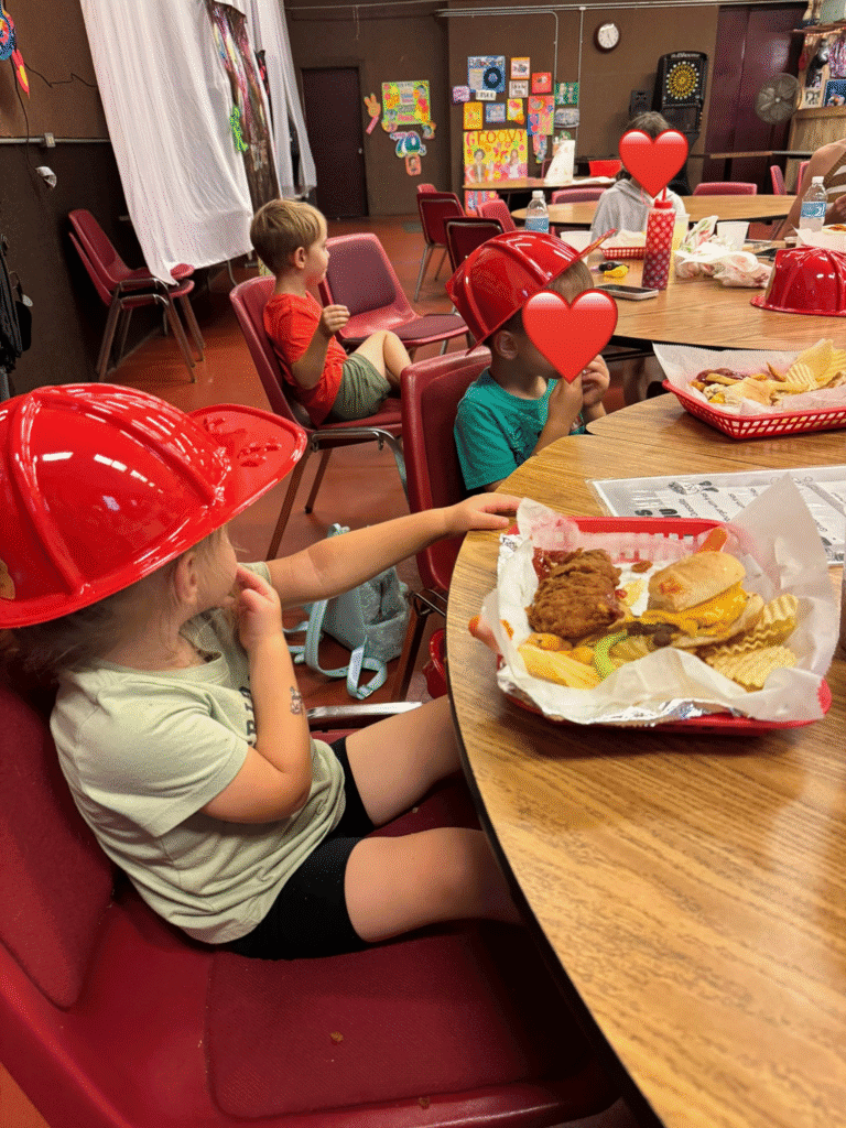 Children wearing plastic red fire hats sit at a table eating burgers and fries at Maxwell Station Restaurant after visiting Olcott Beach Carousel Park.