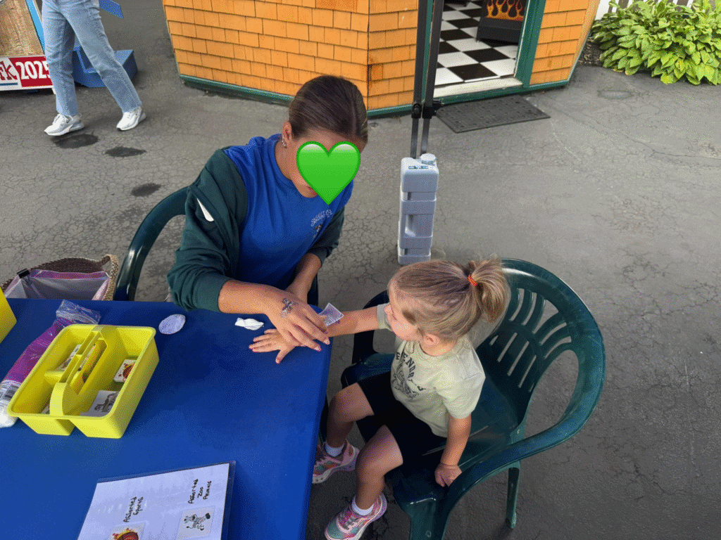 Young girl getting a washable tattoo on her arm from a volunteer at Olcott Beach Carousel Park during the anniversary celebration.