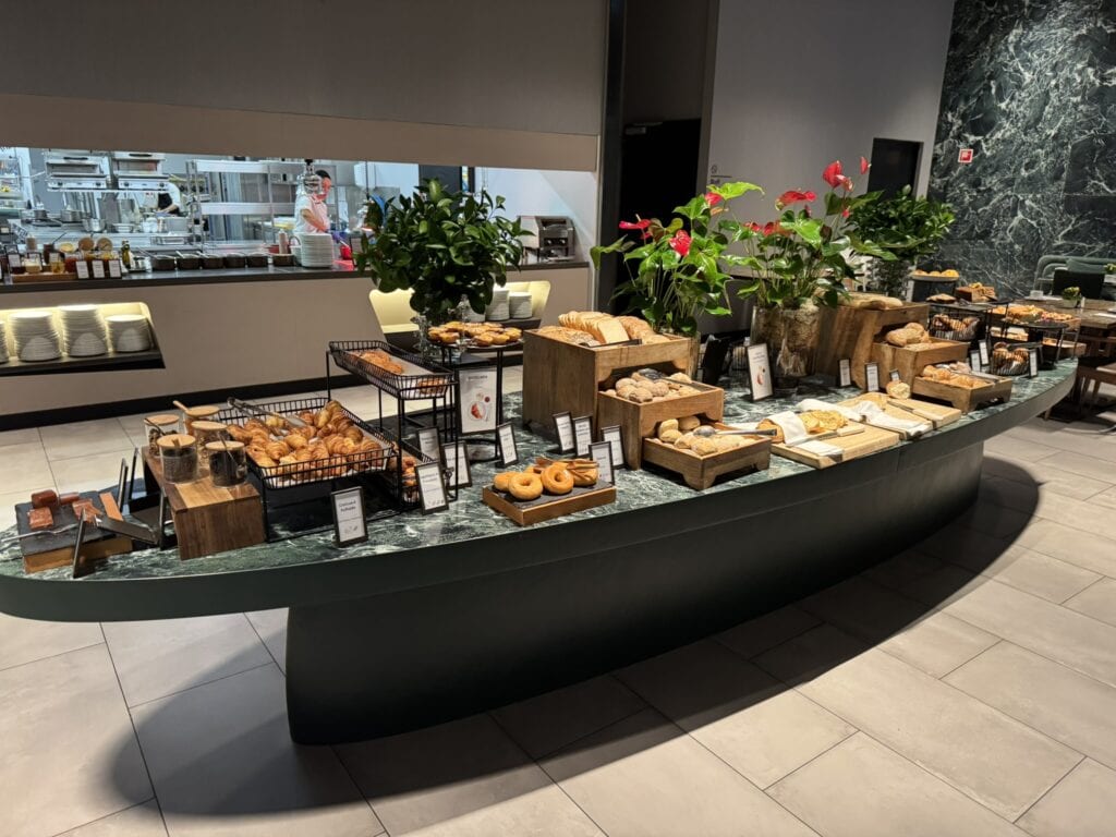 Lavish breakfast buffet at Hilton Porto Gaia featuring a spread of croissants, pastries, artisan breads, doughnuts, and labeled selections in a sleek, modern dining room.