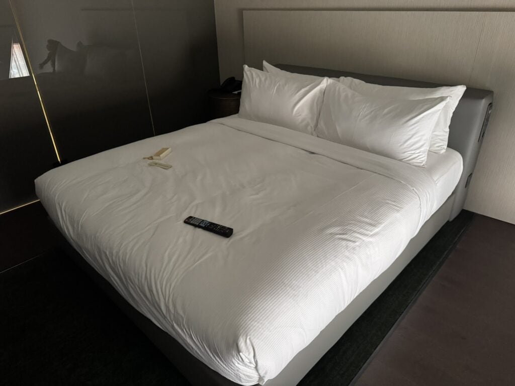 Upstairs view of the Hilton Porto Gaia Family Room suite showing a king-size bed with white linens, a remote control, and a game for the kids arranged neatly on top.