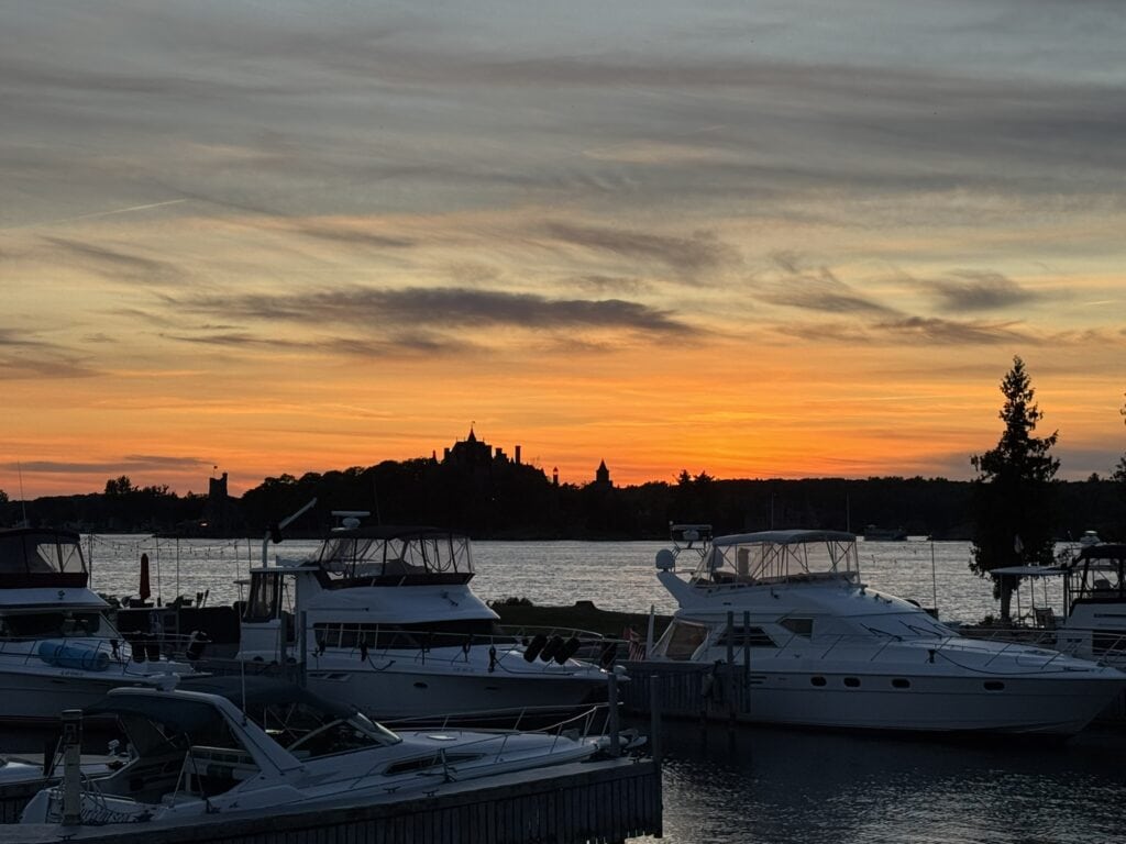 Boats docked on the river with Boldt Castle silhouetted against a vibrant sunset sky in Alexandria Bay.