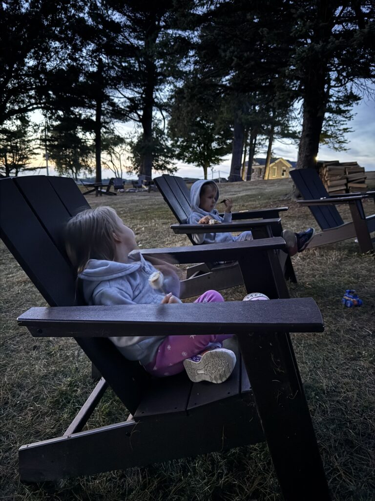 Two young children sitting in Adirondack chairs roasting marshmallows at dusk at The Ledges Resort And Marina.