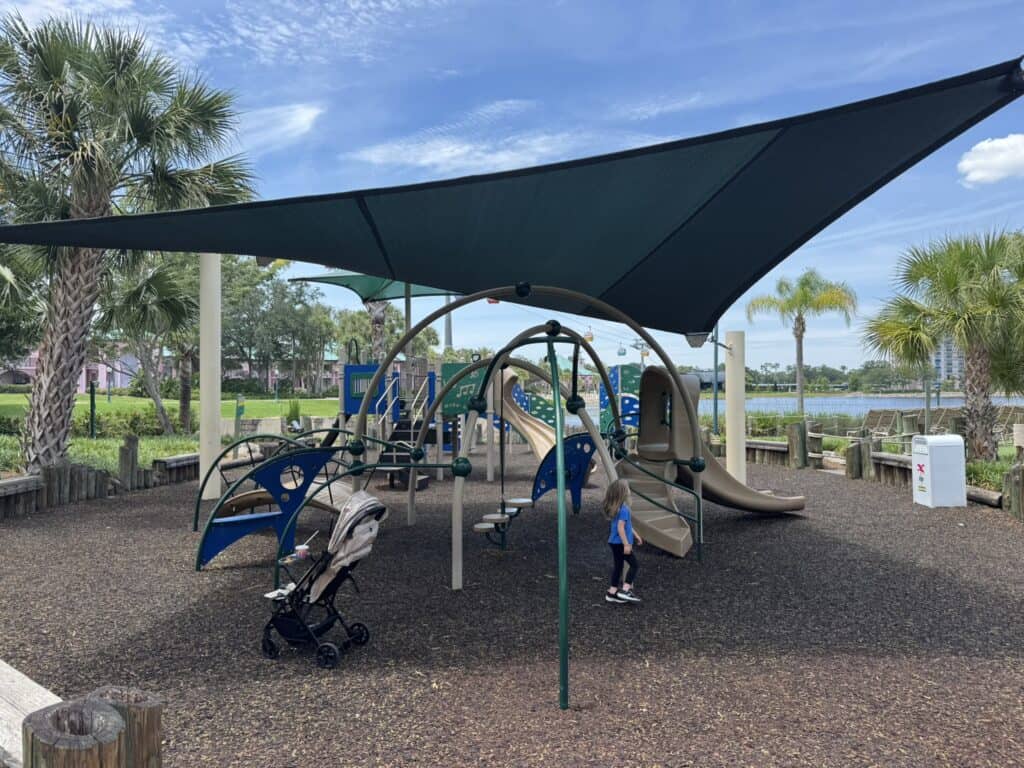 Shaded playground at Disney's Caribbean Beach Resort with climbing structures, slides, and views of Barefoot Bay in the background.