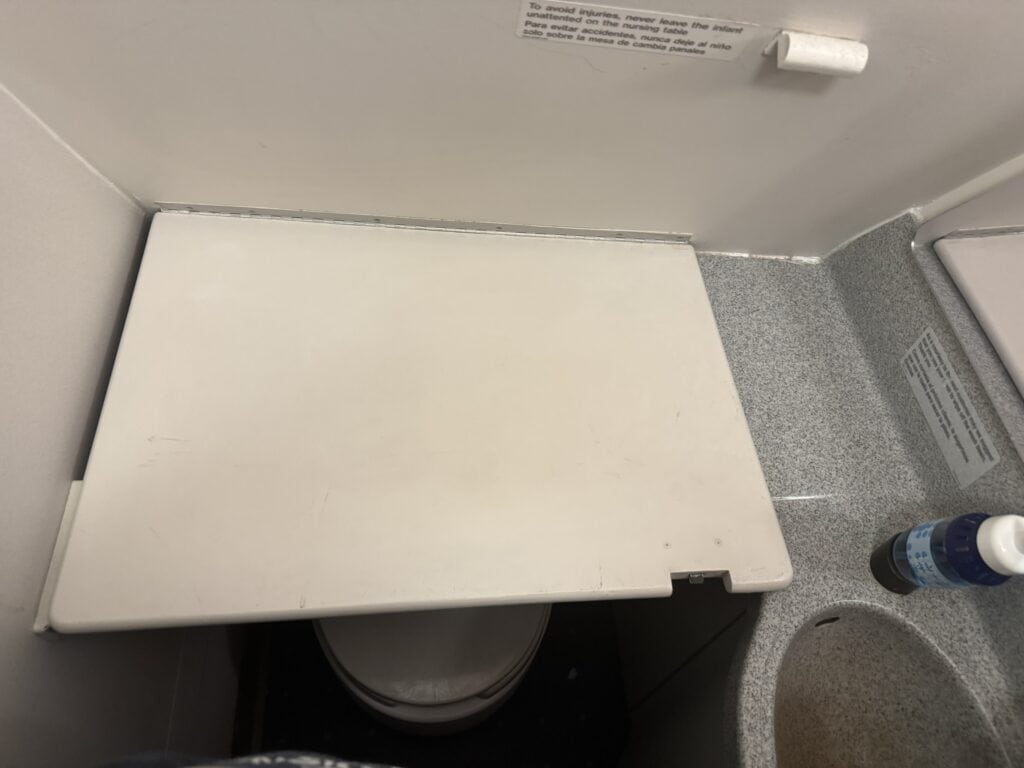Fold-down airplane changing table positioned over the toilet in an airplane lavatory.