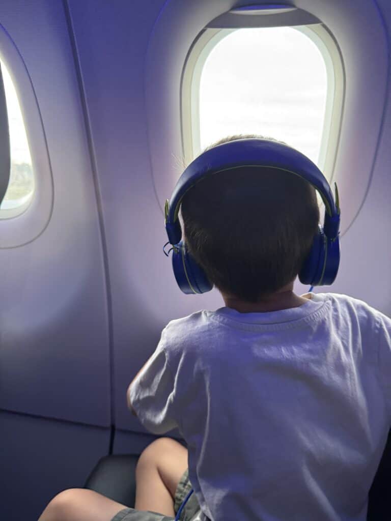 Child wearing blue headphones looking out an airplane window during a family flight