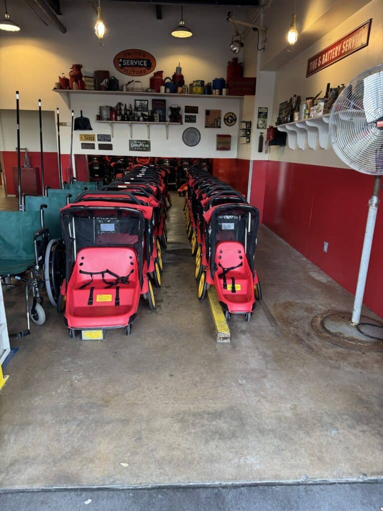 Do you need a stroller at Disney World? Rows of red Disney rental strollers are lined up inside a park rental area.